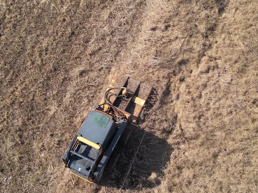 Aerial view of a tractor tilling dry farmland, preparing soil for planting.
