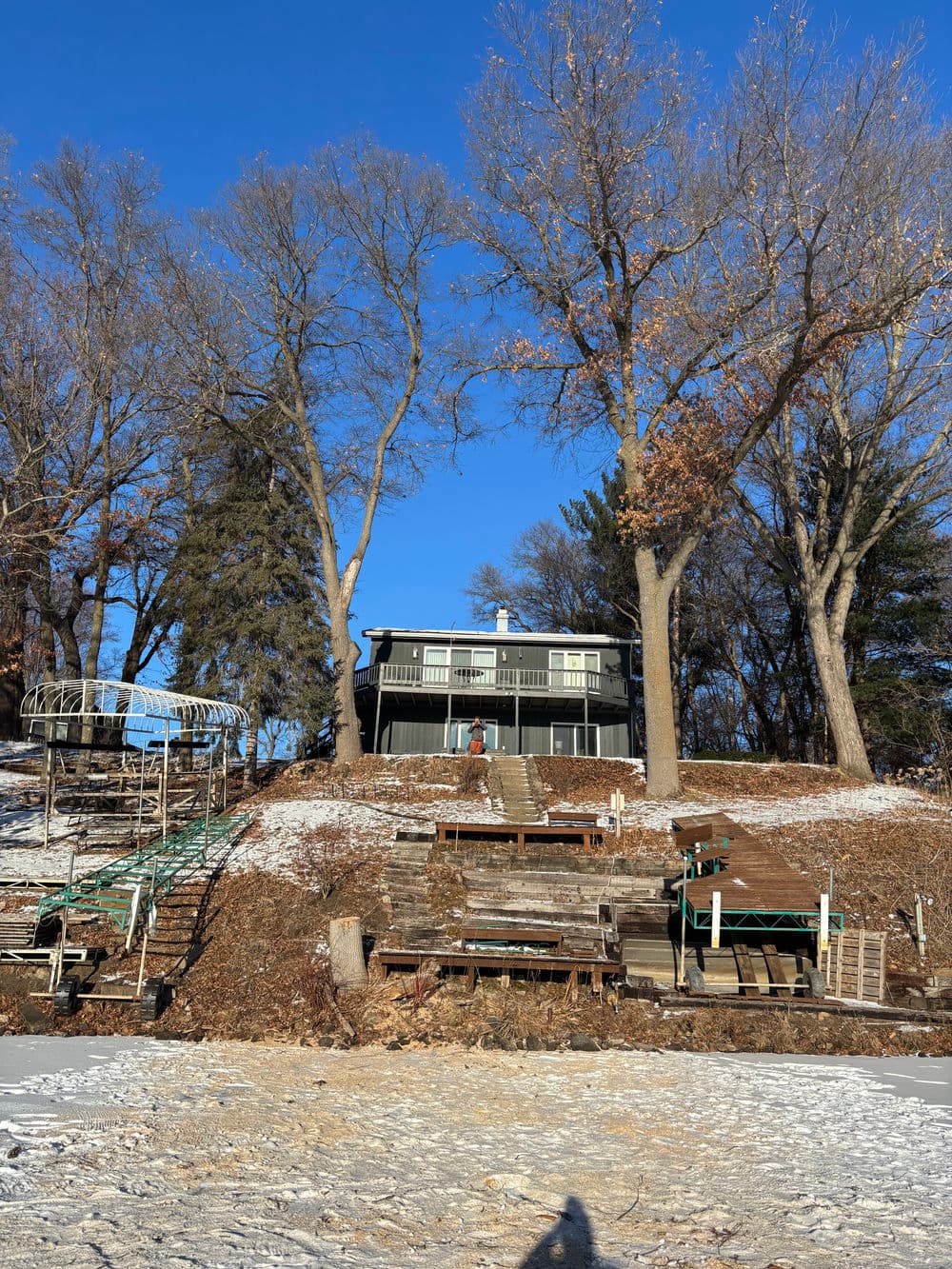 Black house on a hill surrounded by trees, with a snowy landscape and outdoor steps.