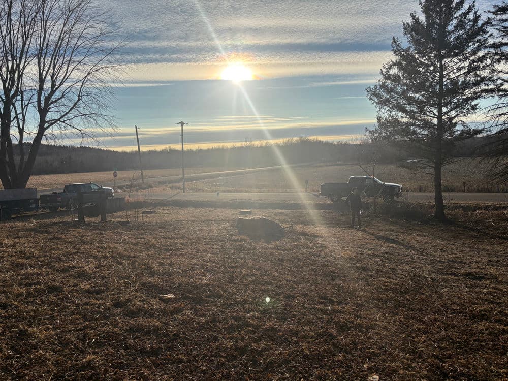 Sunset over a rural landscape with trucks and trees, highlighting a serene countryside scene.