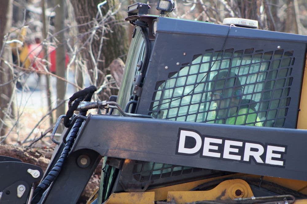 Bobcat loader in wooded area, operator visible through safety mesh window.