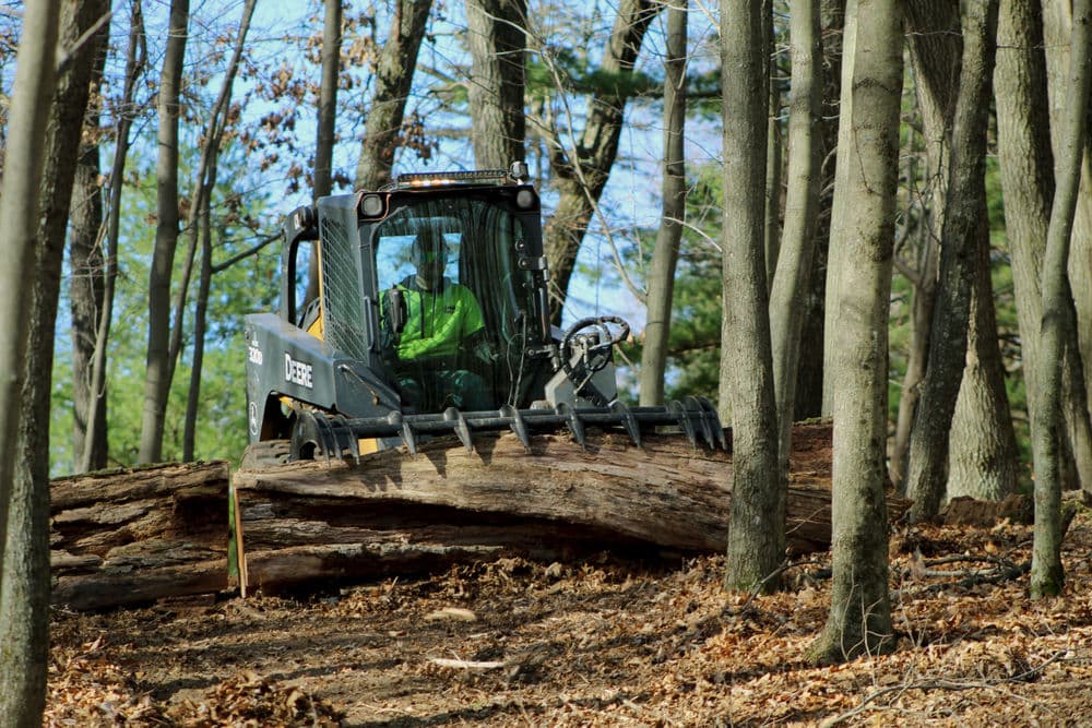 Forestry machine logs clearing in wooded area with operator in green attire.